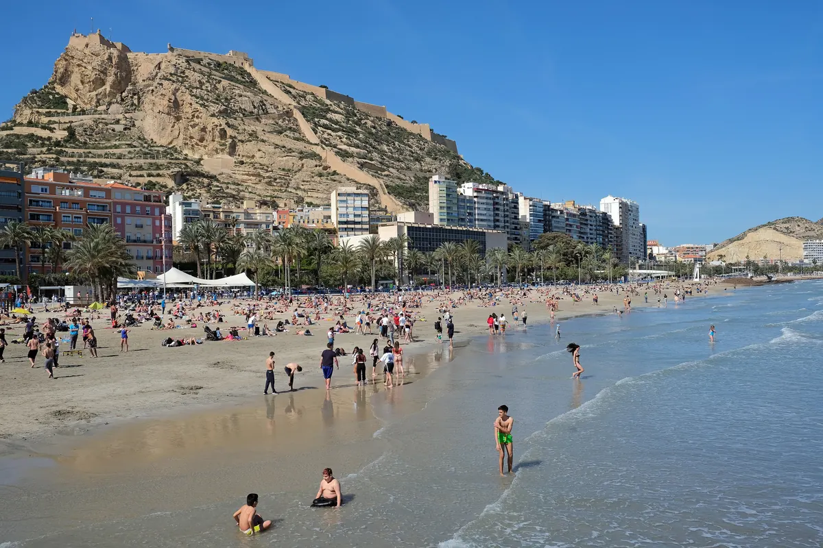 Santa Bárbara Castle on its rocky hill above Postiguet beach in Alicante, with swimmers at the edge of the sea