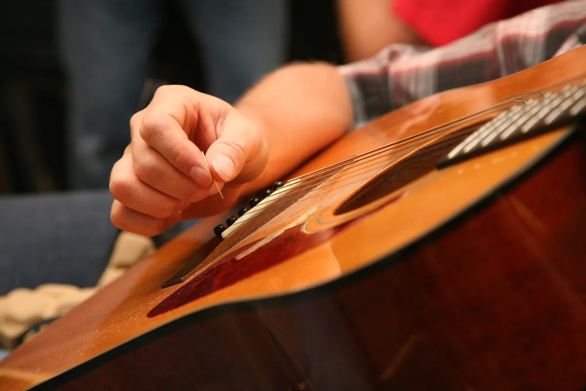 A close view of a hand plucking the strings of a guitar above the sound hole, with the wooden body of the guitar in the foreground