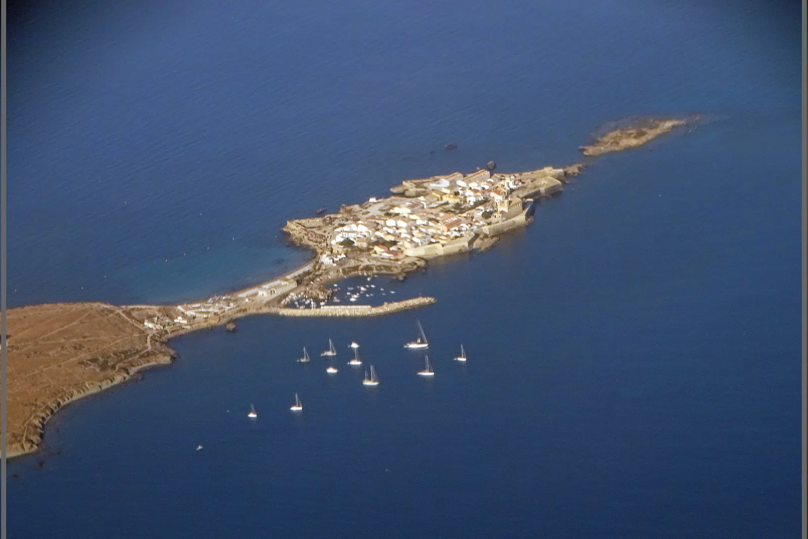 An aerial view of the low, flat island of Tabarca off the Alicante coast, with a small walled town at one end and sailing boats anchored in the blue water